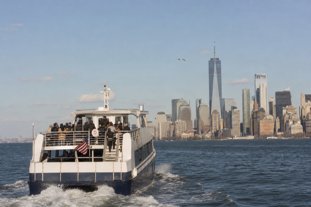 A harbor cruise boat under way in bright afternoon light, passengers on the open upper deck, city towers behind