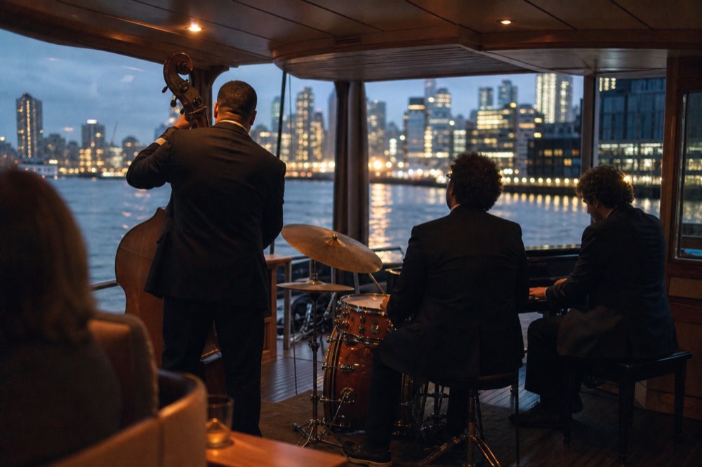 Jazz trio playing in a warmly lit glass-walled yacht saloon with harbor lights outside the windows