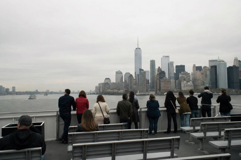 An upper sky deck of a small tour boat with rows of simple seating and a low rail, passengers standing at the front in bright daylight