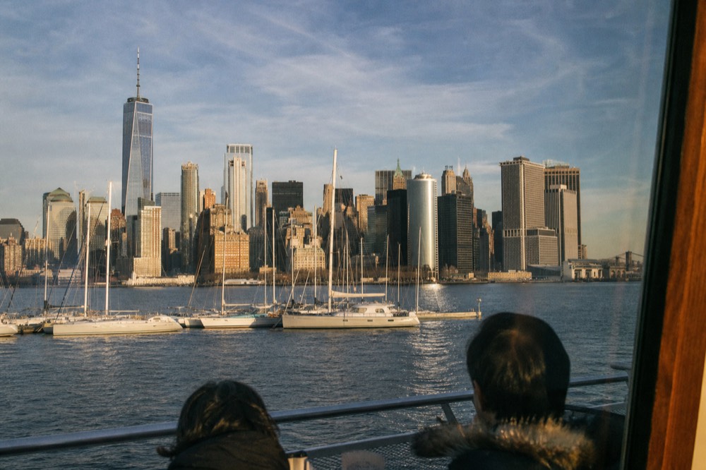 View of the full lower Manhattan skyline seen straight on across open water from a boat deck, marina masts in the foreground