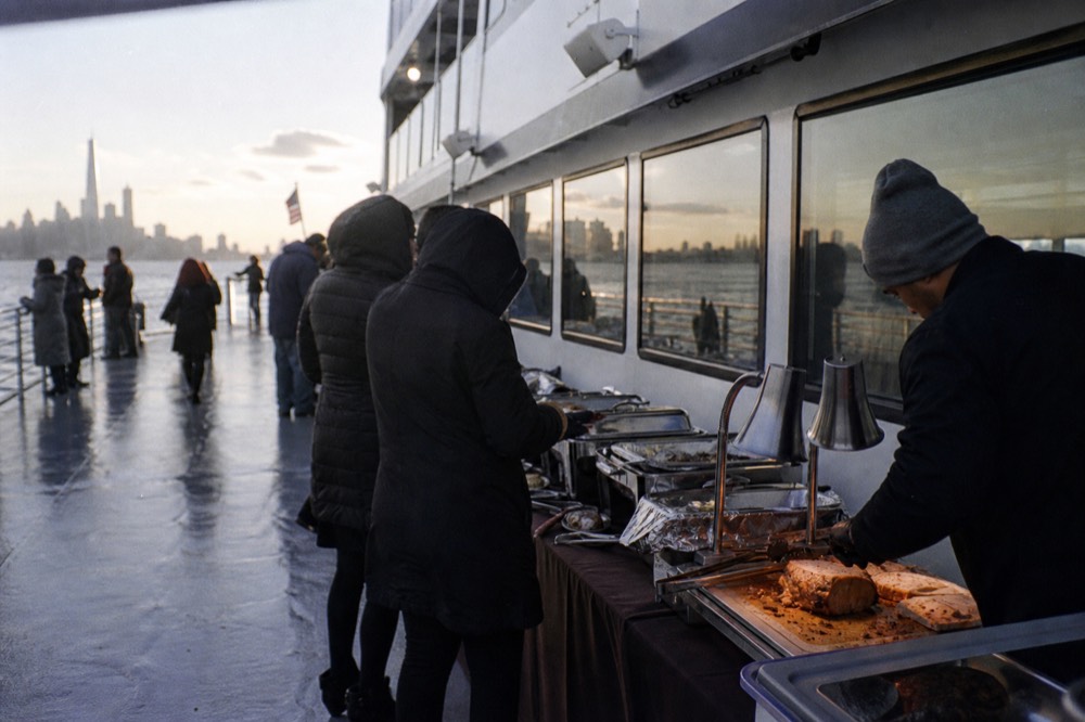 Buffet service line on a boat with chafing dishes and carved meat station, guests serving themselves against a row of windows