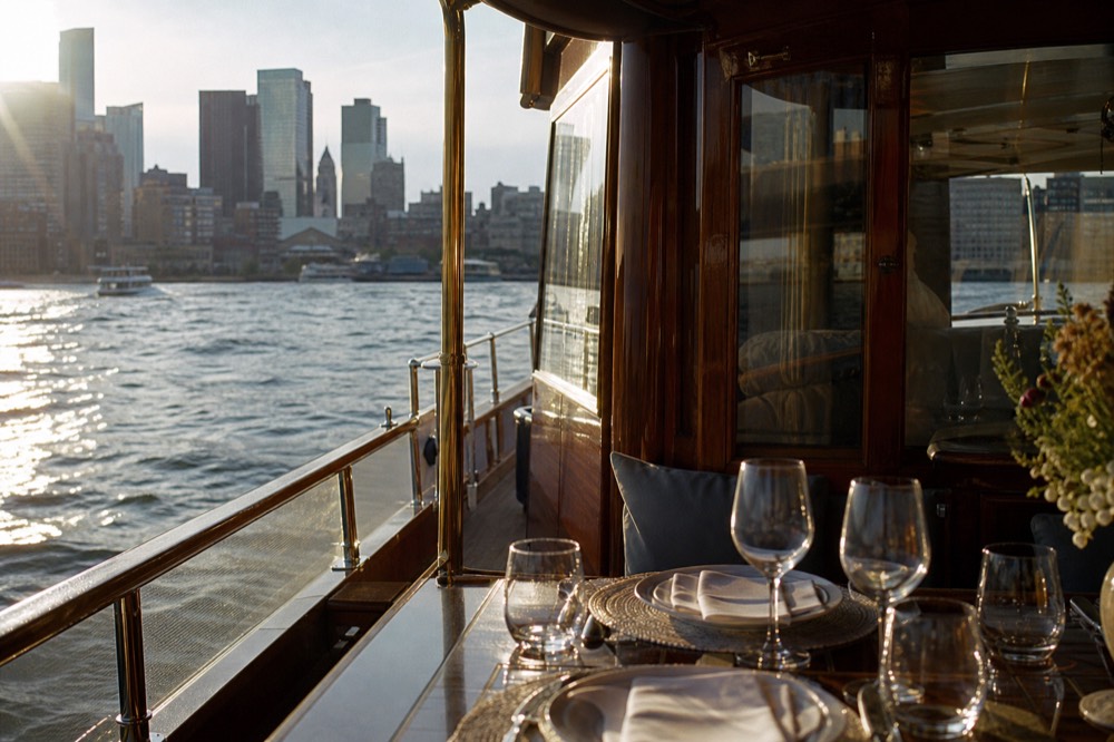 Varnished wooden deck rail and brass fittings of a small classic motor yacht with the Hudson River and low afternoon sun beyond